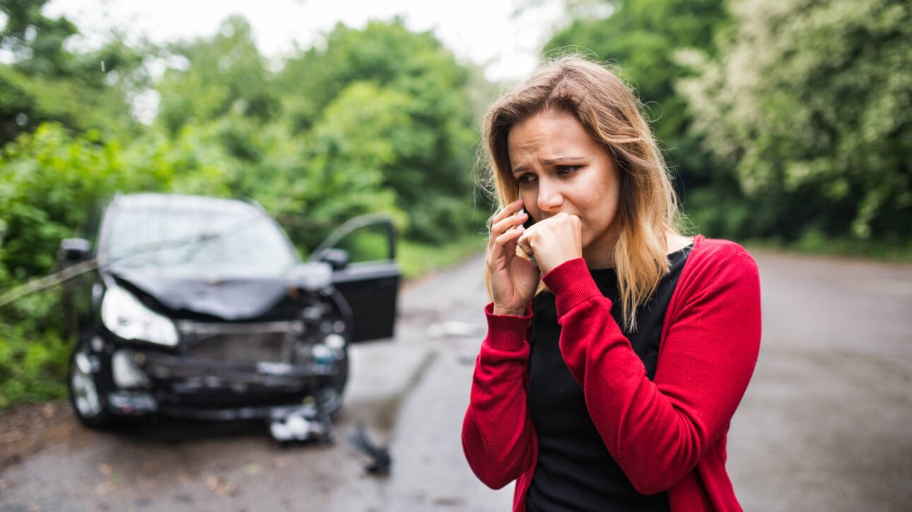 Frustrated woman calling for help on smartphone beside damaged car after accident
