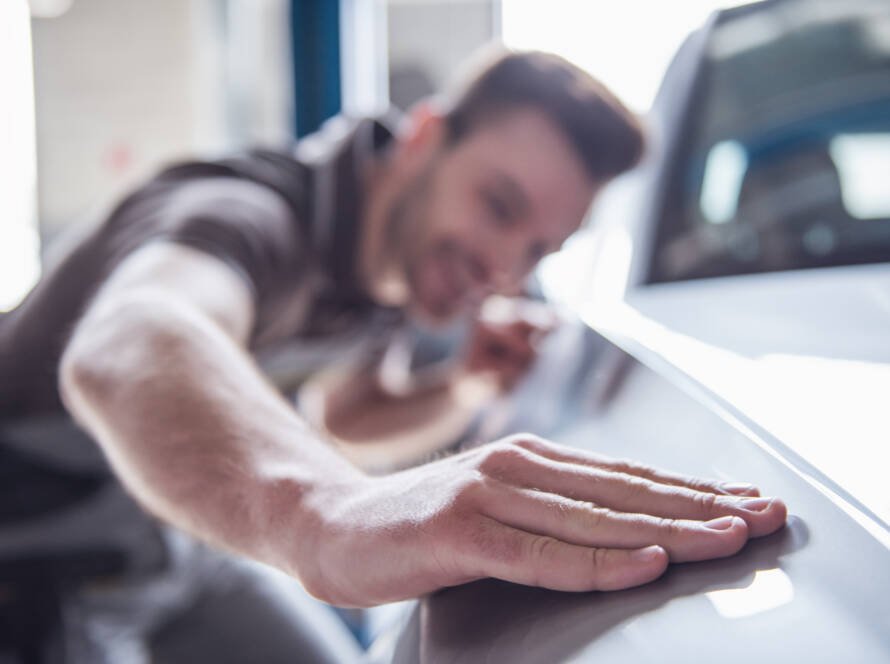Smiling auto mechanic in uniform inspecting car for dents at Elite Auto Body Shop